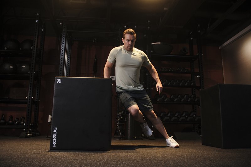 A man in athletic wear performs a lateral movement exercise on a black training platform in a modern gym setting.