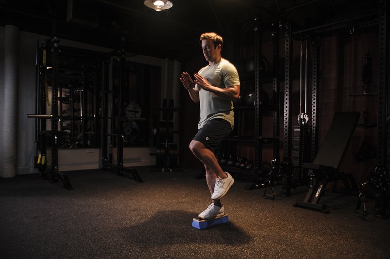 A man in athletic wear performs a dynamic balance exercise on a blue training platform in a modern fitness facility.